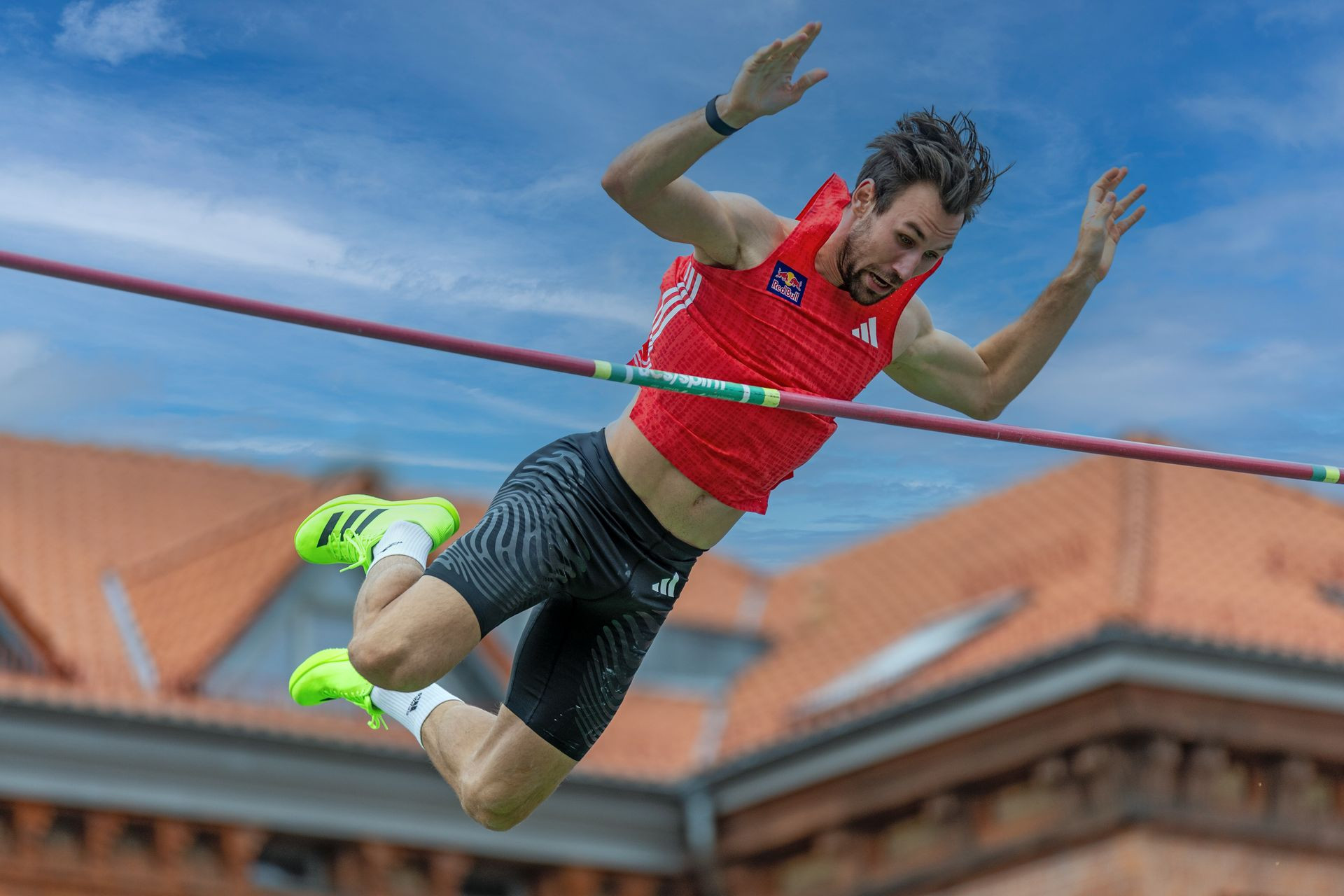Een atleet gaat met gespannen gezicht net over de lat tijdens een polsstokhoogsprong.